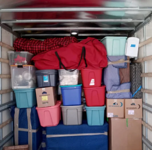 transparent red and blue plastic boxes on top of cardboard boxes inside of a truck
